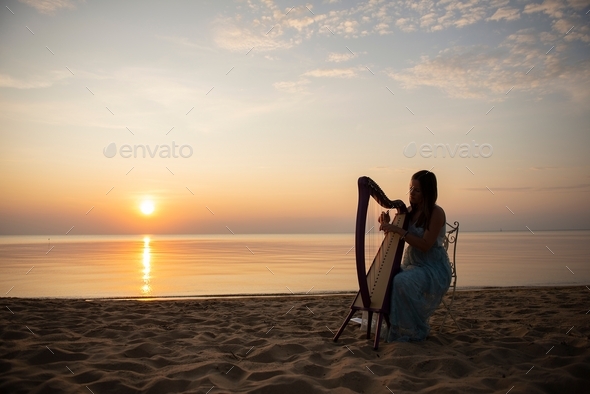 beautiful woman playing celtic harp at beach during sunset