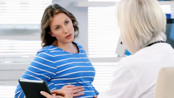 Female doctor interacting over digital tablet with a pregnant woman alt