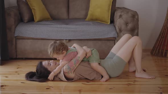 Happy Carefree Mother and Cute Small Child Daughter Tickling Laughing Having Fun Lying on Sofa and alt