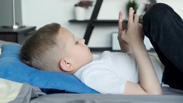 Boy playing mobile game on smartphone on sofa. Preschooler playing mobile phone. Kid using phone alt