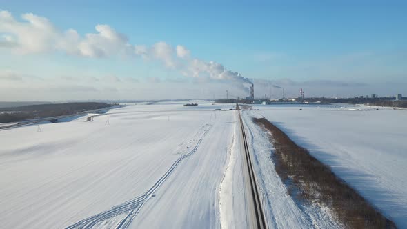 snow-covered road on the background of a factory with smoking pipes top view.