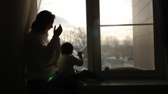Mom and Son Sitting on the Big Window of the House in the Winter alt