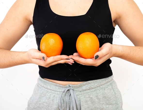 Woman holding two oranges in front of her breast, breast cancer awareness concept
