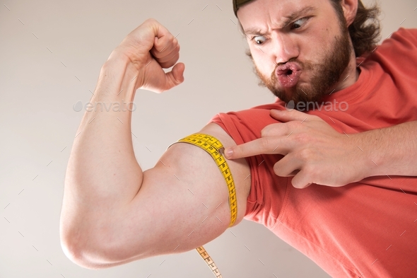 Bearded funny man measuring biceps, muscles of his arm with a yellow tape measure.