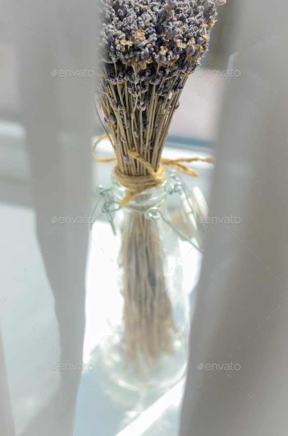 a bouquet of lavender in a craft glass vase against the background of a window through white curtain