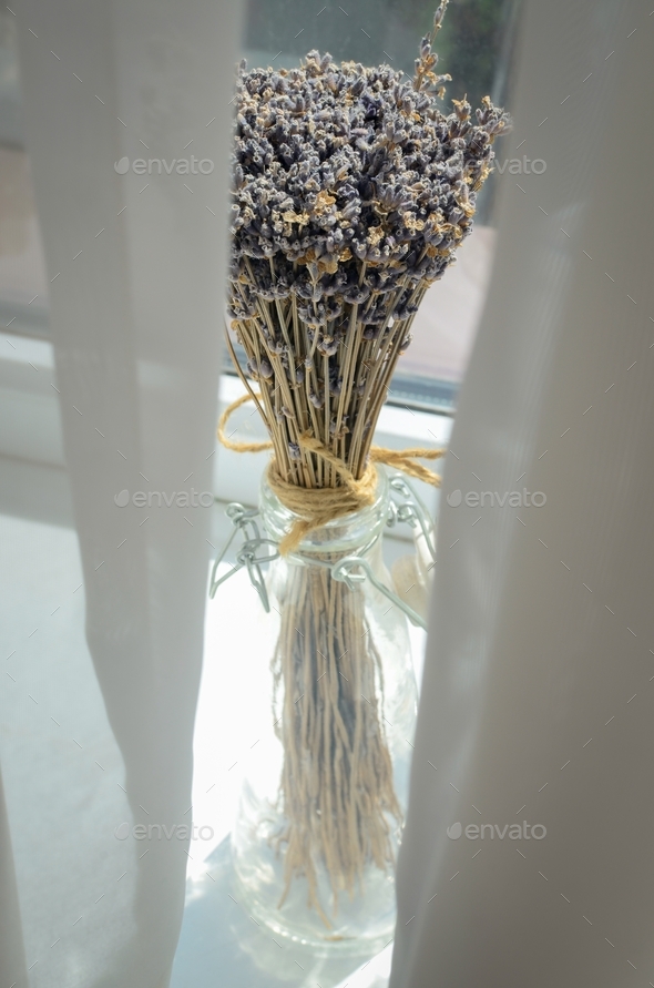 a bouquet of lavender in a craft glass vase against the background of a window through white curtain