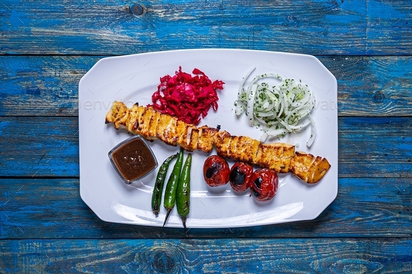 Flat lay chicken kebab on a blue wooden table with grilled tomatoes, grilled peppers