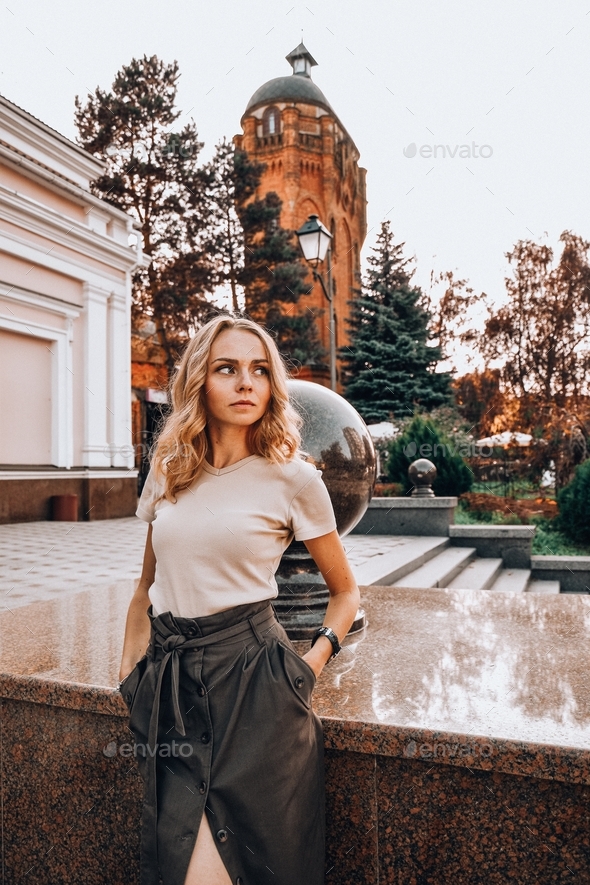 Portrait of young business woman sitting outside. Girl in blouse and skirt on high heels. Blondie