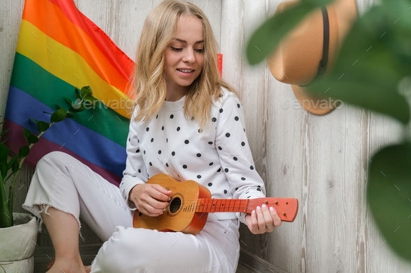 Young millennial hippie woman sitting on balcony play guitar. Music lesson and singer sitting. LGBTQ