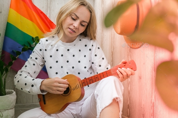 Young millennial hippie woman sitting on balcony play guitar. Music lesson and singer sitting. LGBTQ
