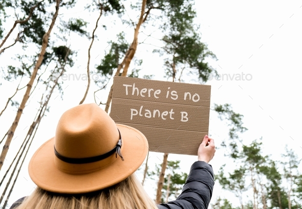 Female hands holding cardboard with text THERE IS NO PLANET B outdoors. Nature background. Protester