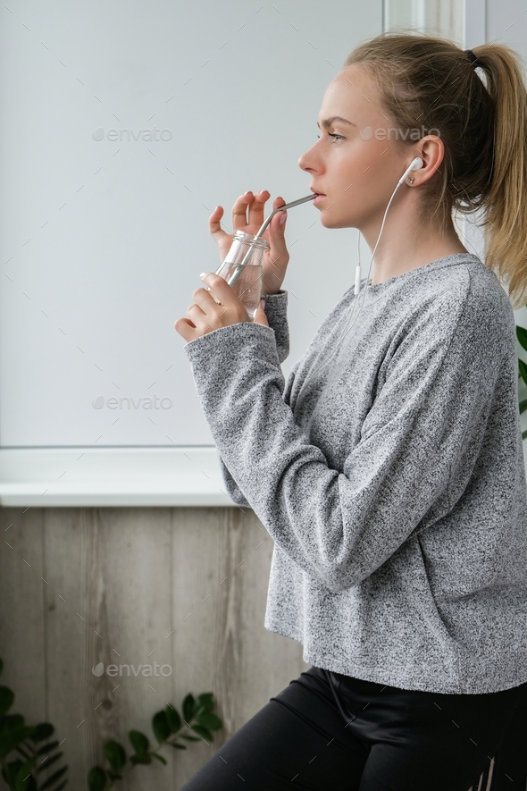 Young millennial blonde woman drinking water from eco bottle with metal reusable straw tube and doin