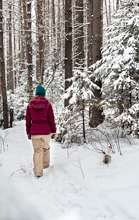 Rear view of a young woman in red jacket walking in winter snowy