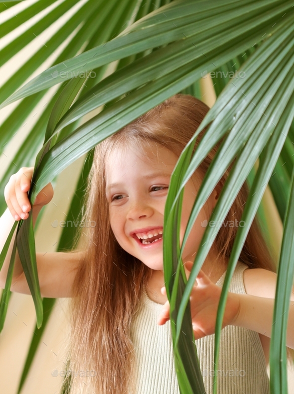 Little girl posing against the backdrop of a palm tree growing at home. Jungle-inspired aesthetics.