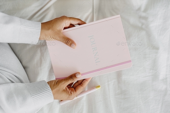Closeup view of woman’s hands holding pink journal.