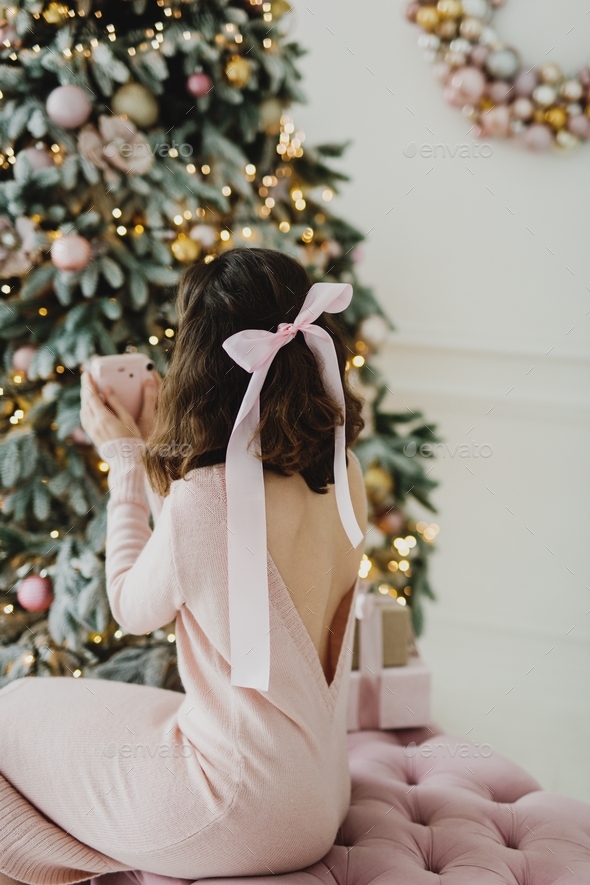 Back view of a young woman in pink dress making photos of Christmas