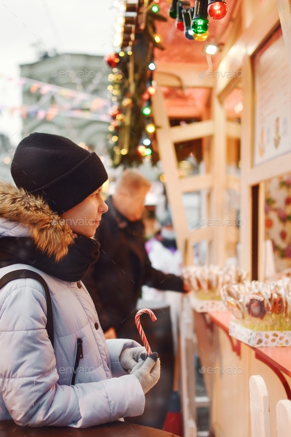 At the Christmas market, a young woman stopped at a candy counter holding a cane lollipop candy.