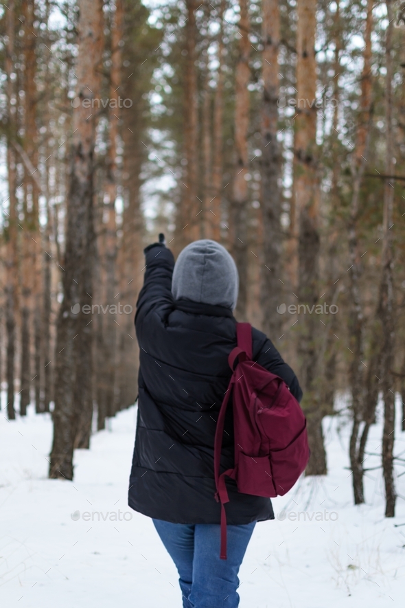 A view of the back of a woman with a backpack, which shows her hand into the depths of the forest.