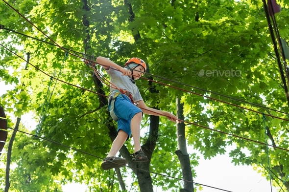 Rope park. A boy in a helmet walks on suspended rope ladders. Carabiners and safety straps. Safety.