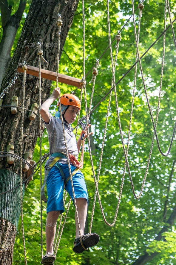 Rope park. A boy in a helmet walks on suspended rope ladders. Carabiners and safety straps. Safety.
