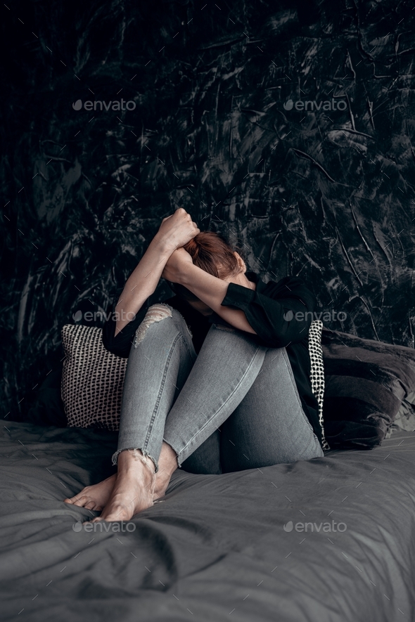Young woman sitting on bed and hugging her knees. Felling bad, sad, depressed.