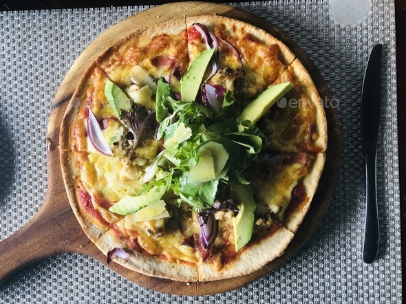 Overhead of pizza with lettuce and avocado on a wood plate  - Stock Photo - Images