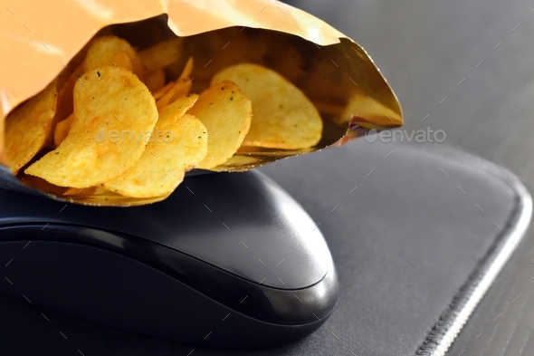 Opened pack of potato crisps or potato chips on a computer mouse. Work from home concept.