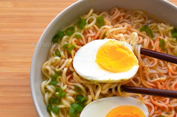 Instant noodles with boiled egg and spring onion in a bowl on a bamboo ...