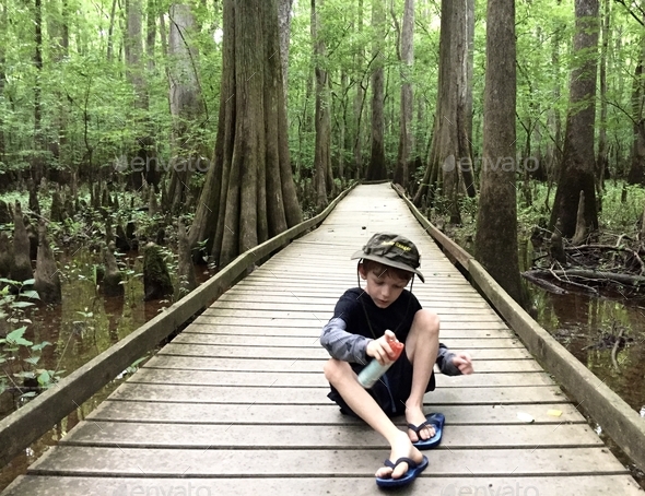 A little boy puts on mosquito spray while walking on a hike through a swamp