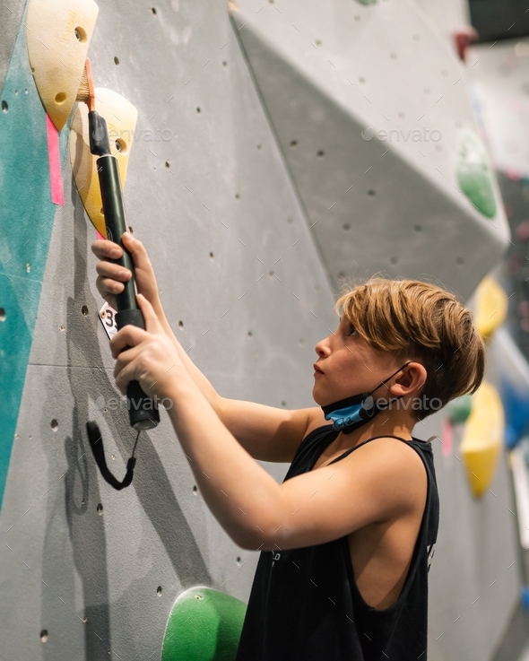 Child brushes chalk off a climbing hold at an indoor bouldering gym