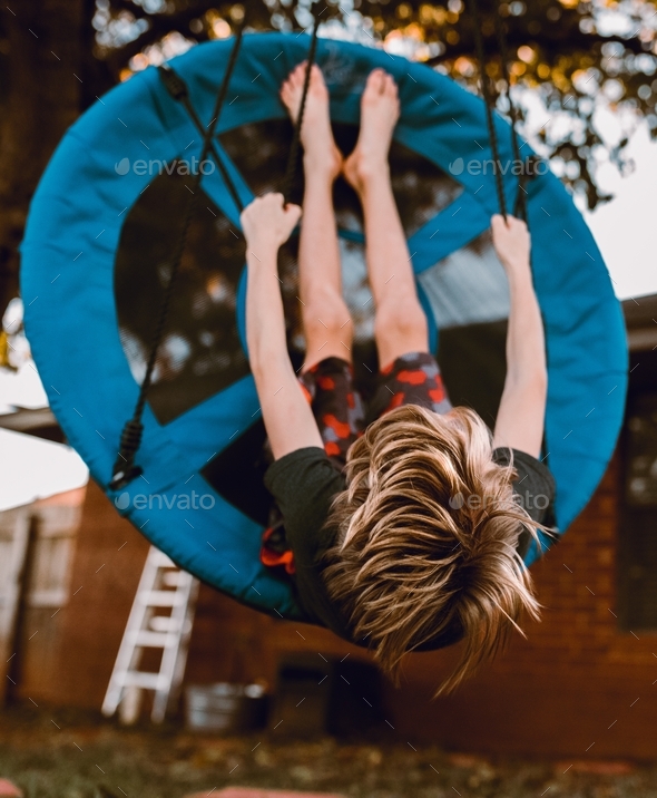 Child playing on a disk swing hanging from a tree in his backyard Stock