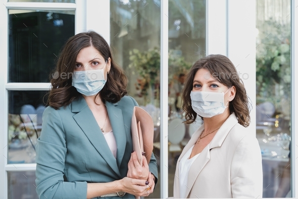 Beautiful women, girls in face masks in stylish suits at entrance to restaurant. Wedding organizers,