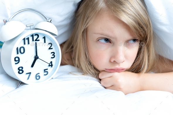 Back to school. Big white alarm,clock. Displeased, sad, unhappy, angry girl, schoolgirl sleeps on pi