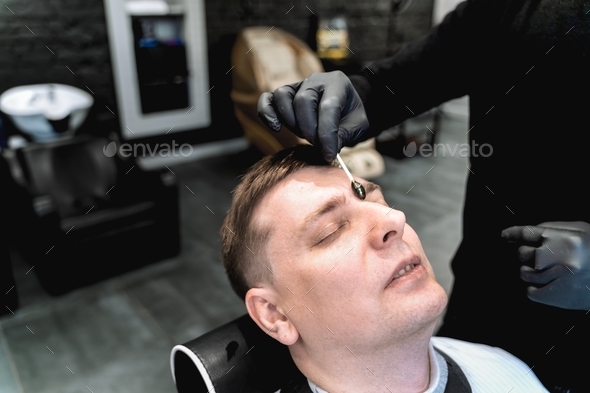 Visit to barbershop.Wax depilation hair removal between the eyebrows.Stylish man makes fashionable h