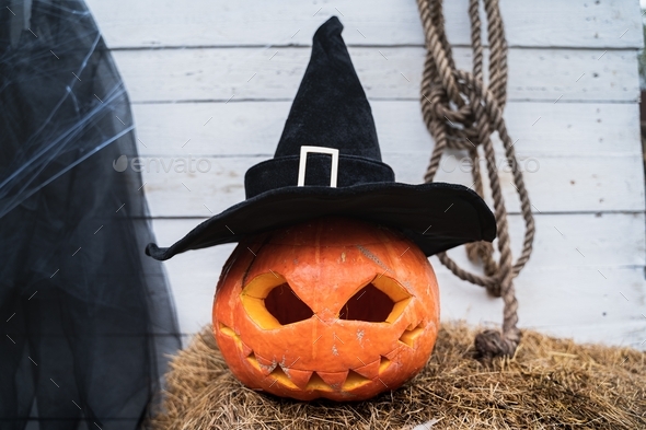 Orange pumpkin for halloween in black witch, wizard hat, jack-o-lantern with scary carved eyes, mout