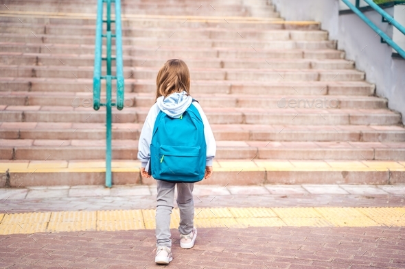 Back to elementary, primary school. Little girl with big backpack goes in hurry, late to first grade