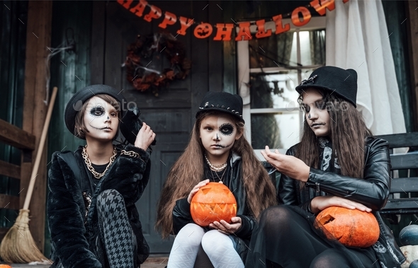 Scary girls,sisters,friends celebrating halloween.Treak or treat game.Pumpkins.Sitting porch steps