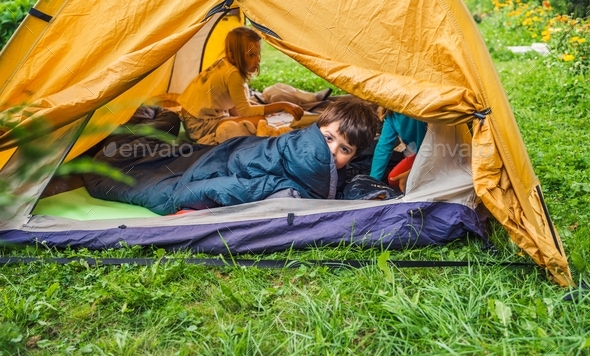 Small children, kids, boy play, sleep in sleepig bag in orange tourist tent. Family trip,hike to nat