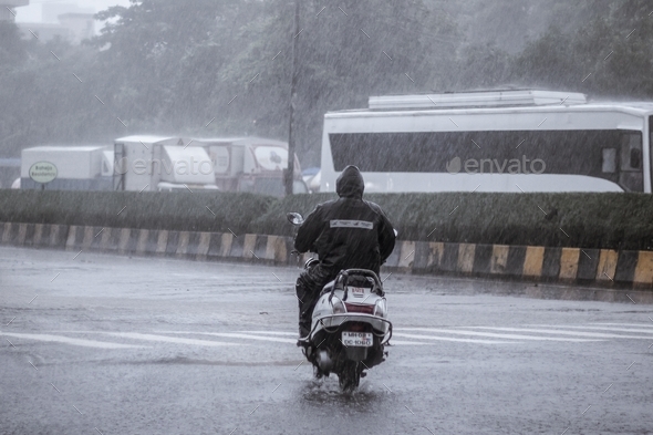 Man riding a two wheeler in heavy rains - Stock Photo - Images