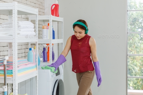 Housework woman listing music by headphone and cleaning washing machine in the laundry room.