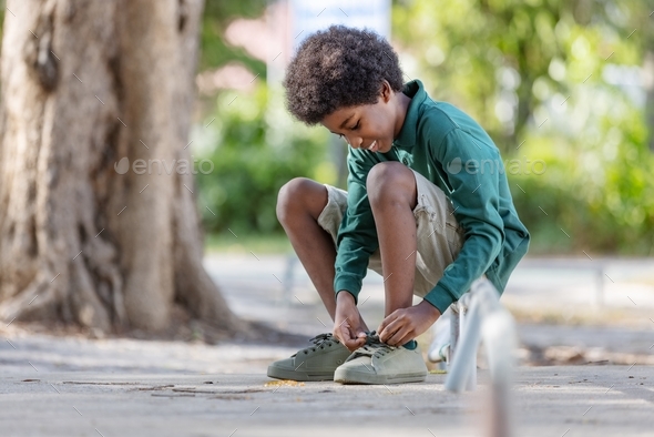 An African black curly haired boy bends down to tie his shoelaces. sitting on the iron railing
