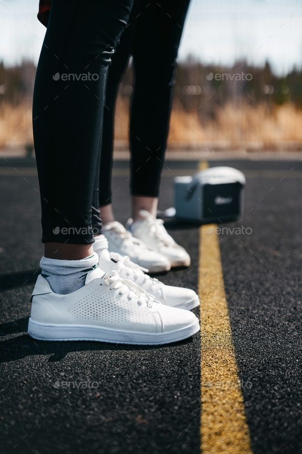 Two persons in white sneakers on the sports ground.