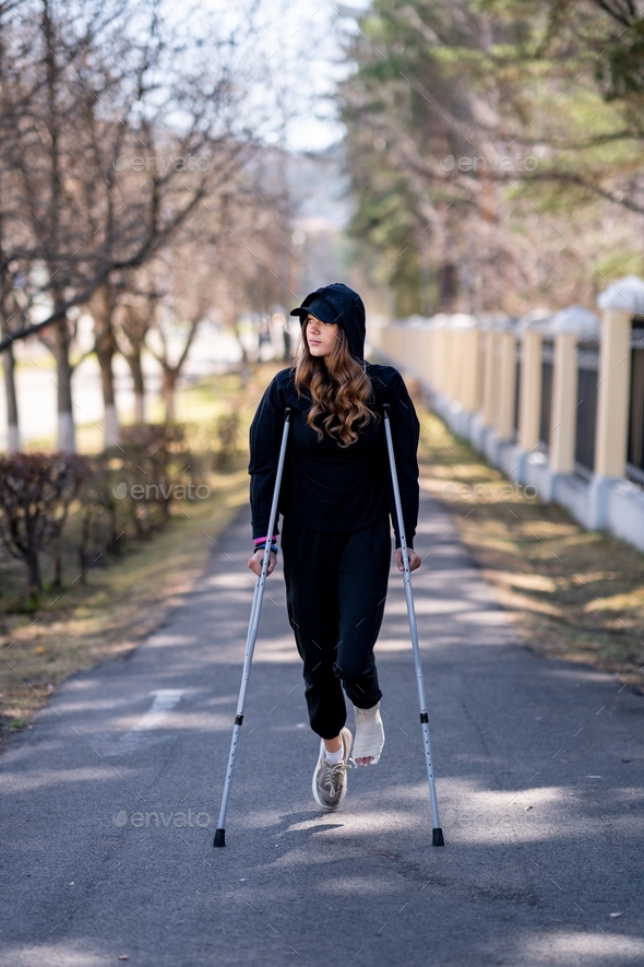  young woman with a broken ankle walks on road.
