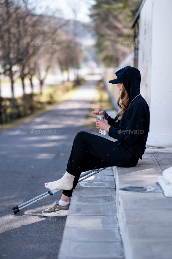 A young woman with a broken ankle sits on the steps.