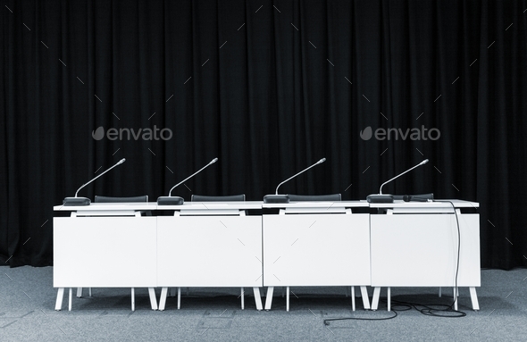 Monochrome picture of conference stand table with microphones in a meeting room