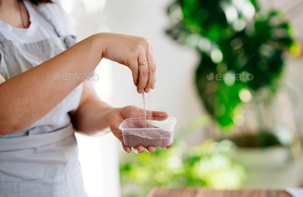 a woman in an apron pours sand into a pot.