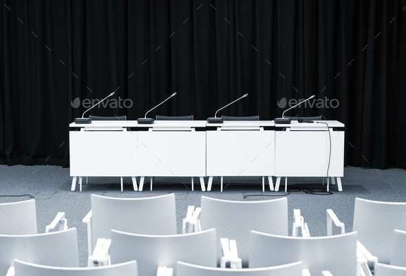Monochrome picture of empty press conference room with seats, stand table and microphones