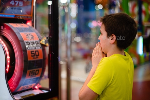 Preteen boy playing a gambling slot machine and expecting to win a jackpot.