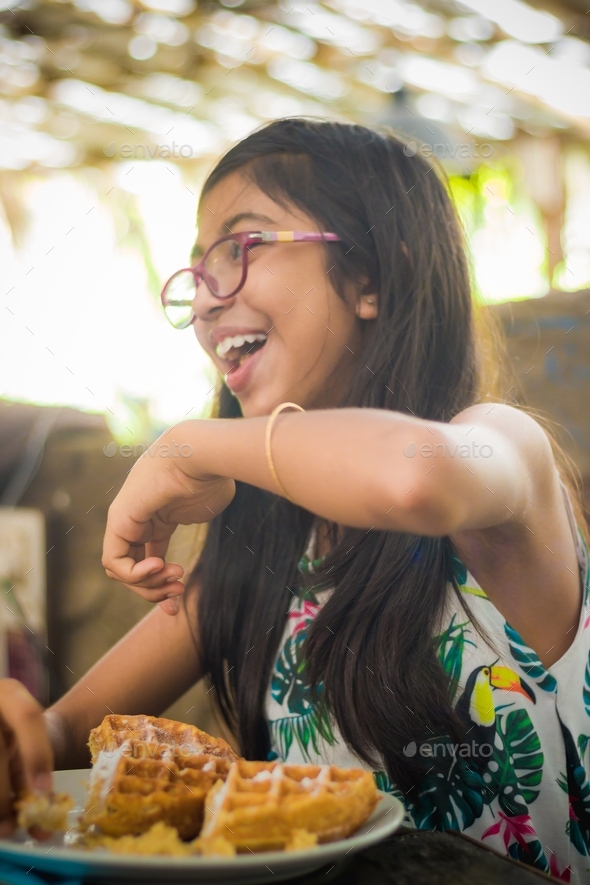 Candid pic of a happy young girl enjoying her breakfast at a restaurant - Stock Photo - Images