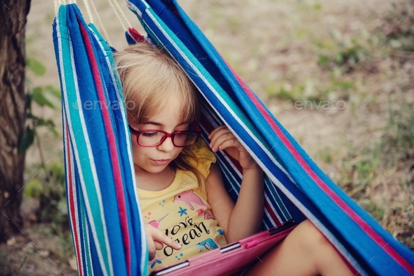 一个戴眼镜的可爱小女孩躺在吊床上用药片库存照片-图像